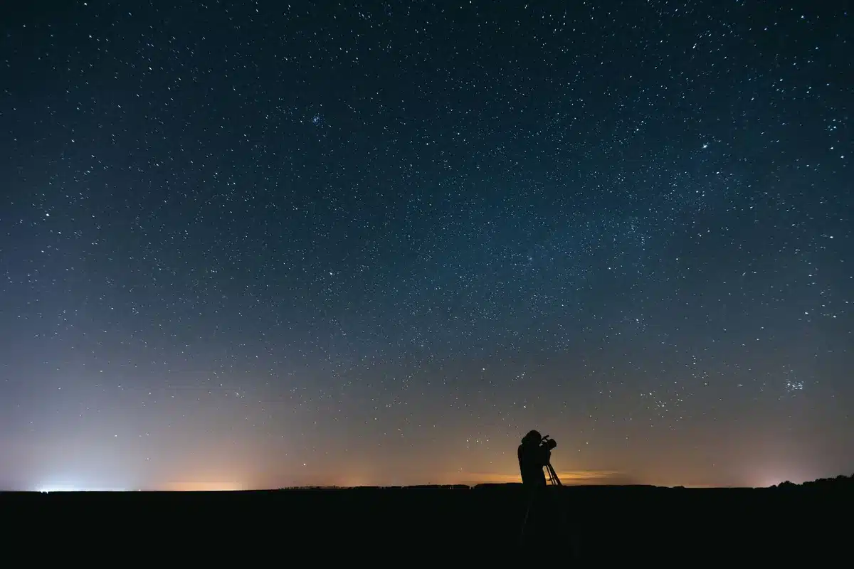 Persona che osserva il cielo notturno con binocolo verso l'orizzonte occidentale