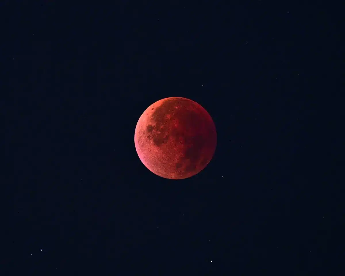 Luna in eclissi con tonalità ramata riflessa sull'acqua scura del mare