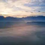 Monastero antico su una montagna nebbiosa con valli himalayane sullo sfondo e bandiere di preghiera al tramonto