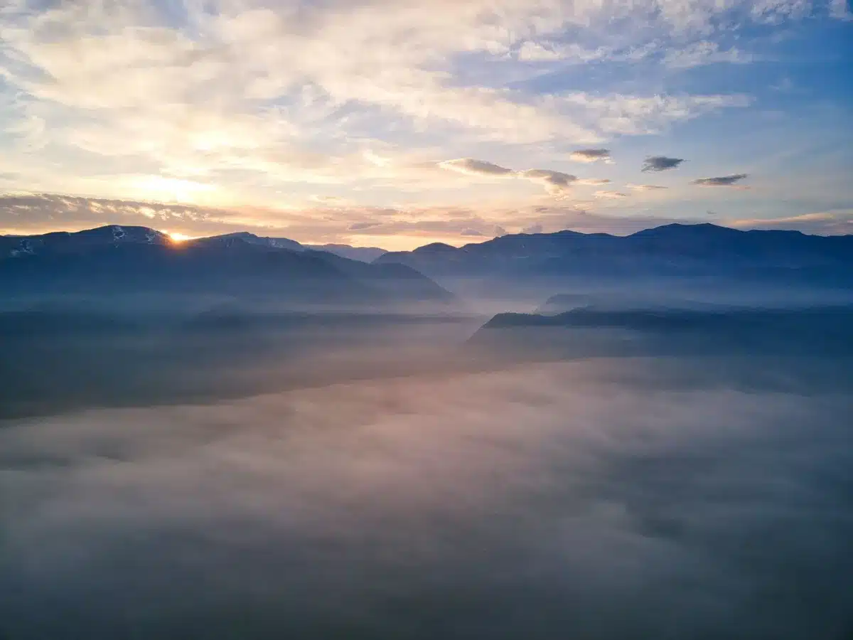 Monastero antico su una montagna nebbiosa con valli himalayane sullo sfondo e bandiere di preghiera al tramonto