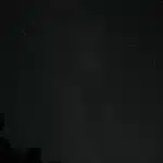 Figura solitaria che guarda il cielo notturno illuminato da scie di meteore luminose