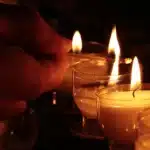 Mani anonime che reggono un copione piegato vicino a una candela commemorativa su un tavolo