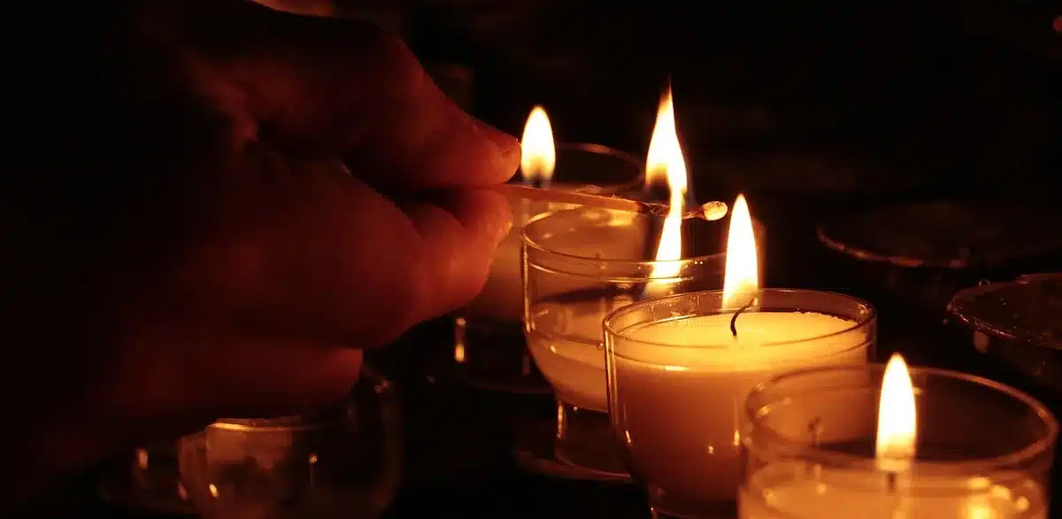 Mani anonime che reggono un copione piegato vicino a una candela commemorativa su un tavolo