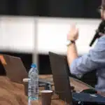 Tavolo di conferenza con sagome di delegati, microfoni e documenti, luce neutra